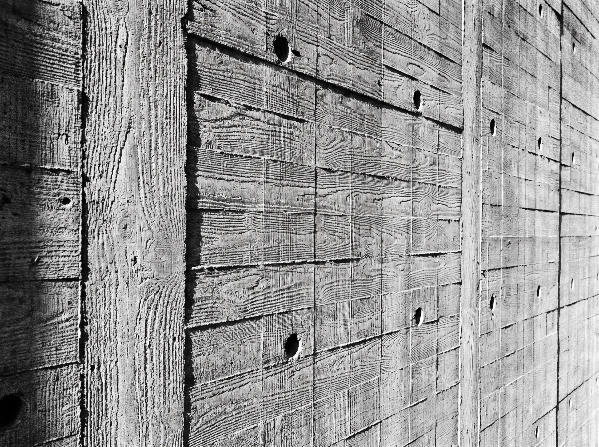 Close-up of raw board-formed concrete texture with visible formwork grain, black and white.