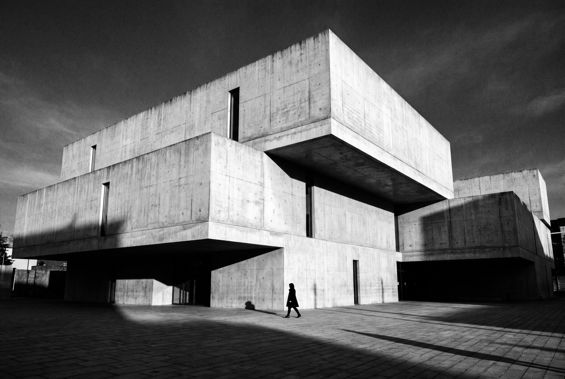 Cantilevered brutalist concrete residence over a plaza, hard side light, black and white.