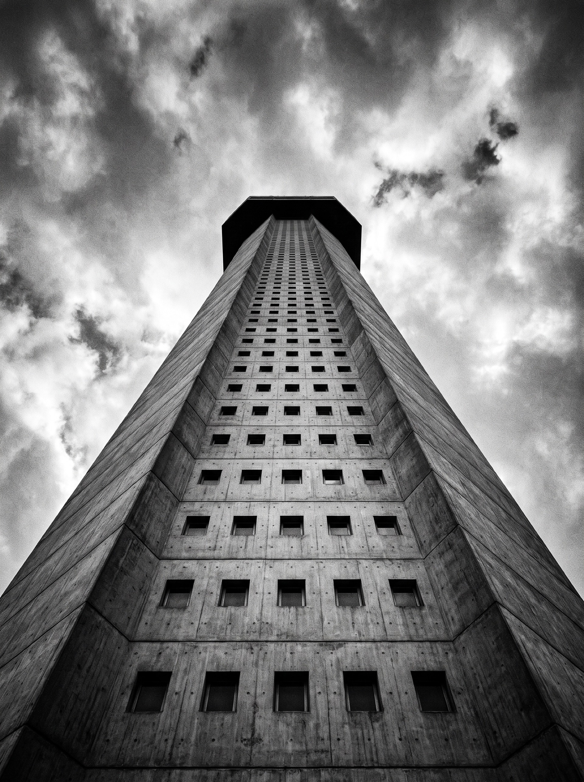Brutalist concrete tower viewed from directly below, converging vertical lines, black and white.